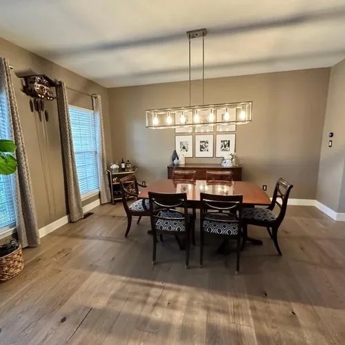 Wide plank wood flooring running through a dining room with a long table and a linear chandelier.